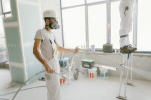 Deux ouvriers du bâtiment portant un équipement de protection et peignant des murs intérieurs pour un projet de rénovation.