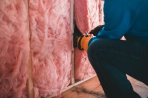 Un ouvrier concentré installe une isolation en fibre de verre rose à l'intérieur d'un bâtiment.