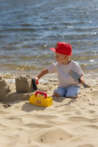 Un jeune garçon construit des châteaux de sable sur une plage ensoleillée avec des outils jouets, montrant de la joie et de la créativité.