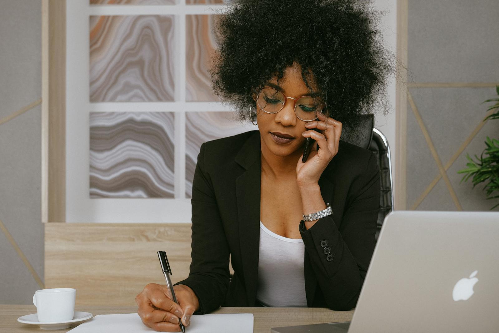Une femme d'affaires passe un appel téléphonique tout en travaillant au bureau, concentrée et professionnelle.