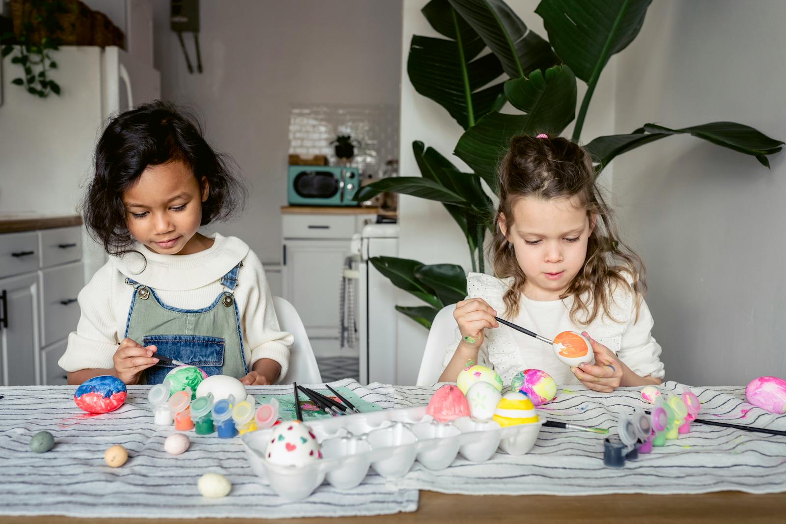 Deux enfants peignent des œufs de Pâques colorés à une table de cuisine.