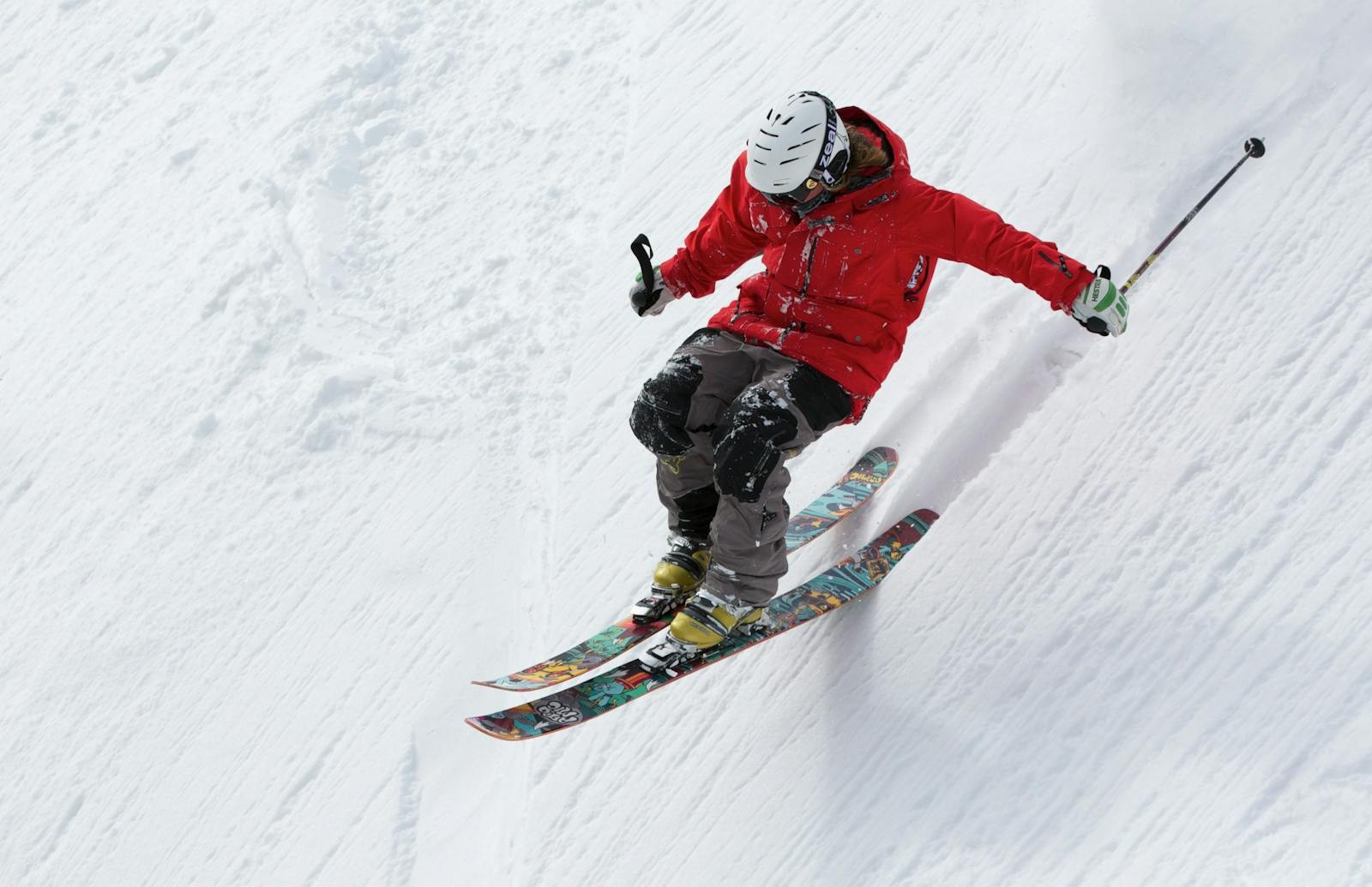 Un skieur vêtu d'une veste rouge descend une pente raide et enneigée, démontrant ainsi son habileté et son aventure dans les sports d'hiver.