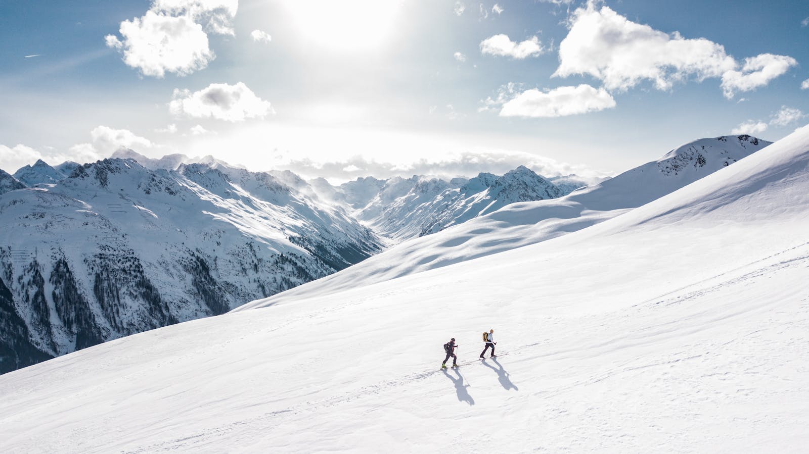 Deux skieurs gravissant une pente de montagne enneigée et ensoleillée à Ischgl, en Autriche, pendant l'hiver.